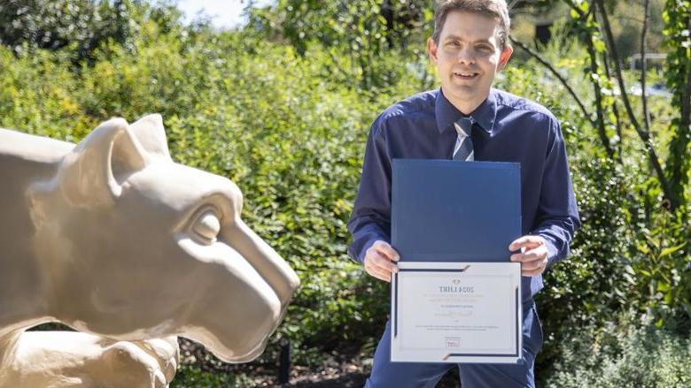 Brett Spencer holding award next to Nittany Lion statue
